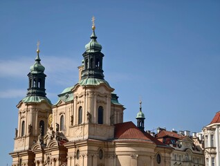 Fototapeta premium Sunlit sandstone facades surround green domes. Bright blue sky highlights historic towers and rooftops