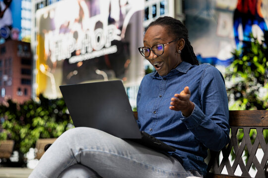 Laughing, laptop and jolly woman outdoors watching funny movie, having fun. Enjoying relaxation time, notebook and African american girl outside amused by hilarious comedy TV show