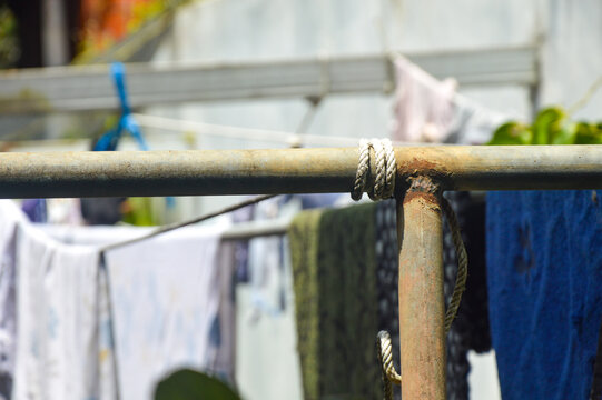 Close up of rope tied to a rusty metal pole for clothesline. Macro detail of weathered iron pipe and cord texture. Domestic laundry equipment background.