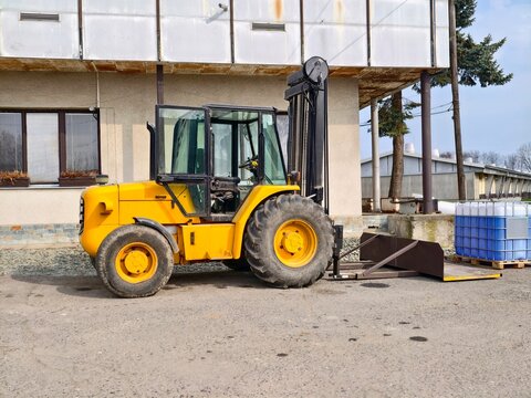 Yellow forklift stands idle outside factory. Loading bay forklift with crates in industrial yard