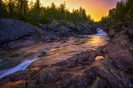 Sunset view of Pollfoss waterfall flowing through a rocky gorge on the Framruste River, surrounded by forest in Billingdalen, Oppland, Norway.
