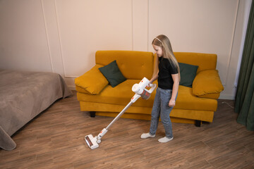 Little girl cleaning the floor in a modern living room while using a cordless stick vacuum cleaner, performing domestic chores and learning household responsibilities for a tidy home © Volha
