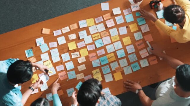 Top down view of smart project manager pointing at sticky note on meeting table with sticky notes. Skilled business team with casual outfit planning and working and choosing marketing idea. Symposium.
