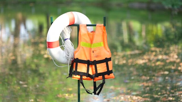 Orange life jacket and white lifebuoy safety gear for water rescue near river pond lake outdoor emergency flotation device