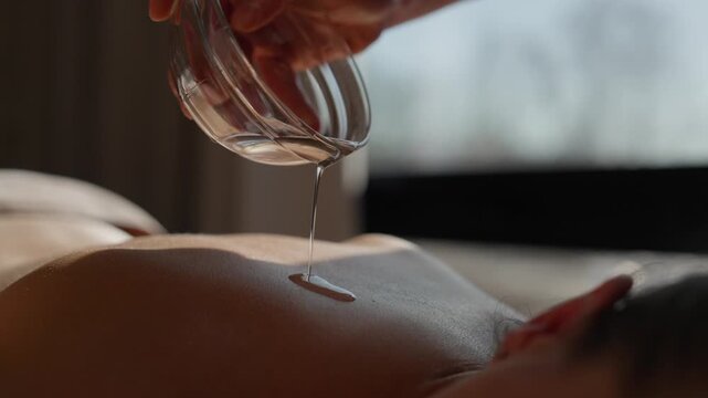 Closeup of relaxing spa massage session with warm aromatic oil gently poured onto bare back, highlighting soothing wellness treatment and tranquil body care ambiance