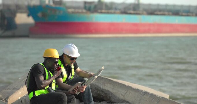 Engineer and technician review port operations and coastal logistics beside the waterfront in daylight, supporting maritime planning, cargo monitoring, and harbor infrastructure assessment.
