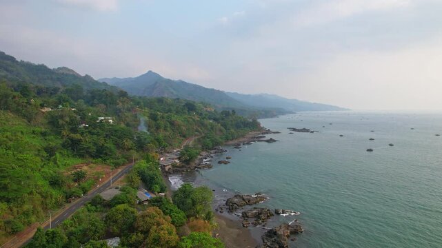 Aerial drone footage of the road going until Ciletuh Geopark, from Pelabuhan Ratu, Sukabumi regency, Java island, Indonesia, with the rocky beaches along, blue sea waters, and fishing wooden huts