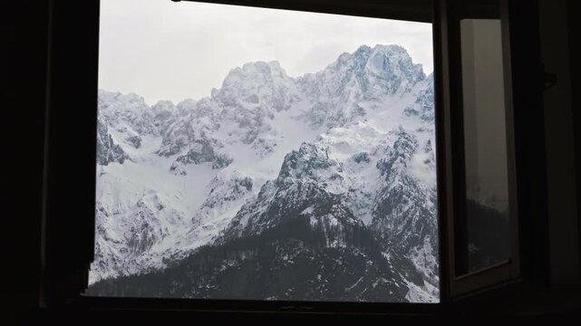 Stunning view of the majestic Julian Alps in Slovenia, seen from the inside looking out through the window of a cozy alpine mountain cottage.