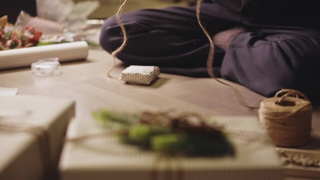 Hands Gently Secure Twine and Pine Sprigs on a Wrapped Gift - Close Up