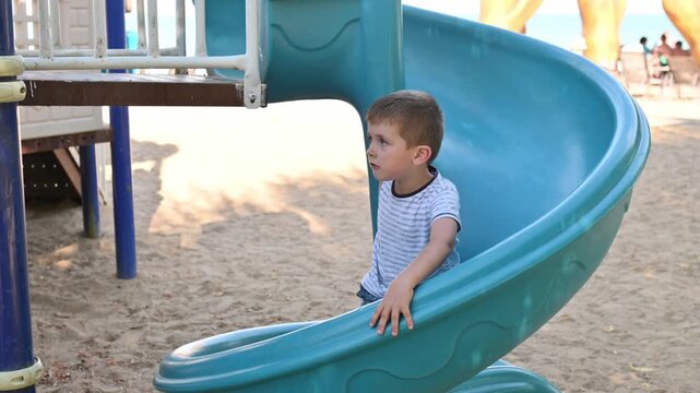 A boy slides down a hill in a park in summer