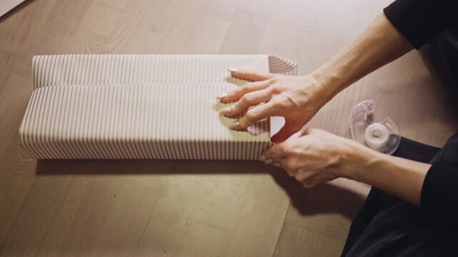 Hands Smooth and Tape Striped Wrapping Paper Neatly Around a Christmas Gift - High Angle Shot