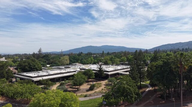 Aerial drone footage flying backwards revealing the lush, green campus of West Valley College in Saratoga, California, with the Santa Cruz Mountains visible in the background on a sunny day