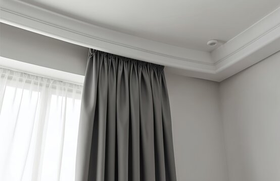 Interior close up of modern room window with grey curtains and sheer white fabric panels. Ceiling cornice detail with subtle lighting creates elegant ambiance. Clean lines emphasize minimalist decor.
