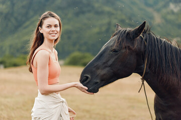 Obraz premium A young woman in a coral top gently touches a dark horse in a rural field, smiling softly as the animal nuzzles her hand, creating a warm, natural bond between human and horse.