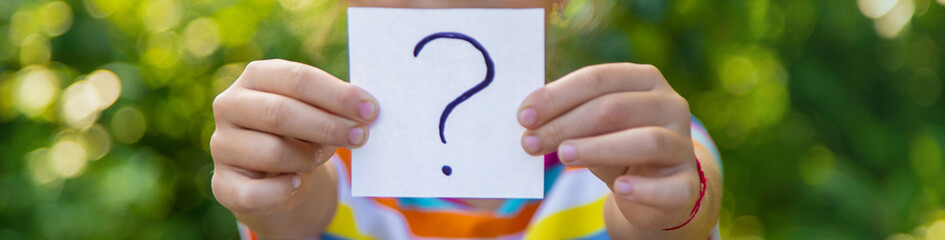 The child holds a paper with a question mark. Selective focus.