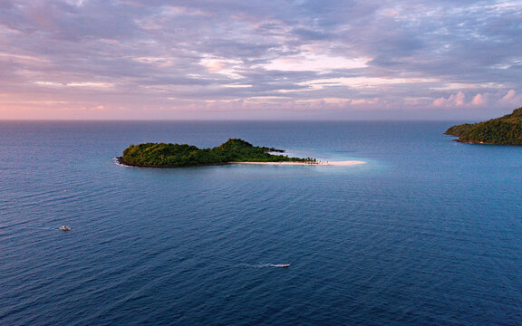Aerial view of a secluded island paradise with lush greenery meeting the soft white sand under a pastel sky, Concepcion, Western Visayas, Philippines.