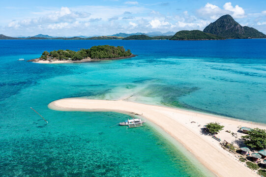 Aerial view of a pristine sandbar stretching into turquoise waters, connecting to a lush island paradise under a bright sky, Concepcion, Western Visayas, Philippines.