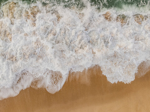 Aerial view of the shoreline where golden sands meet the frothy turquoise waves, creating a mesmerizing dance of color and texture, Quiaios Beach, Figueira da Foz, Portugal.