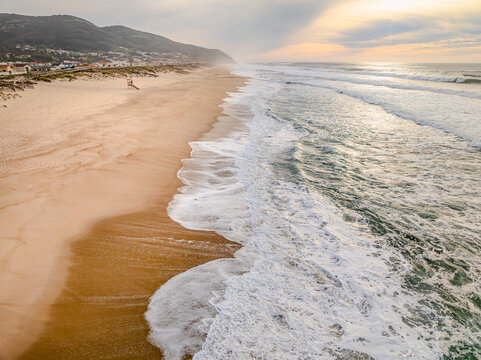 Aerial view of golden sands meeting the frothy turquoise waves under a soft, pastel sky, Vila Nova de Gaia, Portugal.
