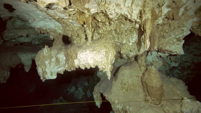 Rows of mineral stalactites hang from the ceiling of a submerged limestone cave with clear water in Cenote Dos Ojos, Quintana Roo