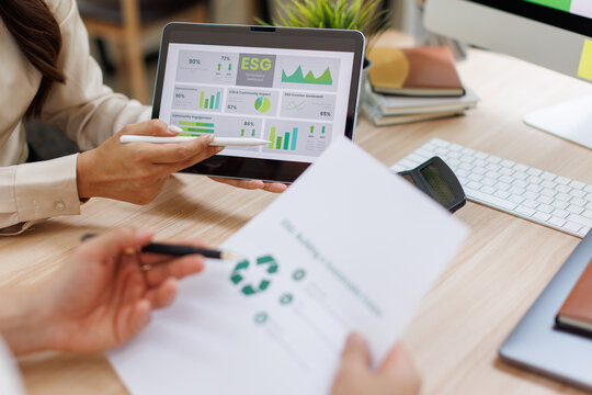 Asian Professionals Reviewing "Building a Sustainable Future" Report Analyzing Environmental Impact Data and Green Dashboard  in Modern Office