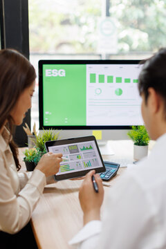 Asian Professionals Reviewing "Building a Sustainable Future" Report Analyzing Environmental Impact Data and Green Dashboard  in Modern Office