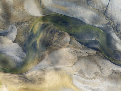 Aerial view of winding waterways carve through the earth, blending muted yellows and greens into the sandy landscape, Walvis Bay, Erongo Region, Namibia.