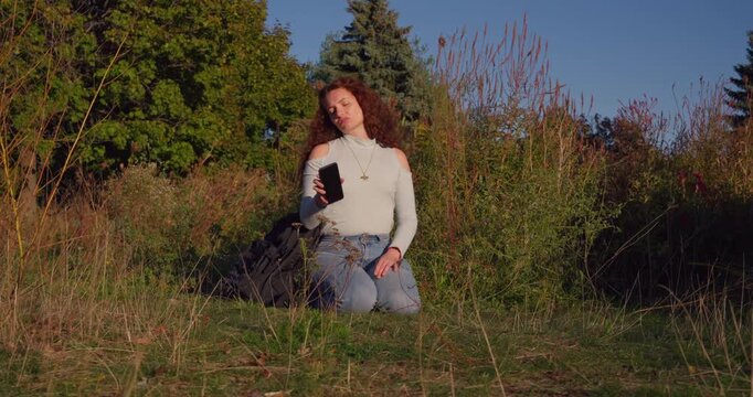 In warm late afternoon light, a young woman buries her smartphone in a field, making a decisive symbolic break from screen dependence and digital overload.
