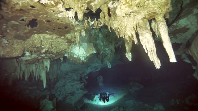 A cave diver approaches an air pocket beneath a ceiling of stalactites inside a submerged cavern system in Cenote Dos Ojos