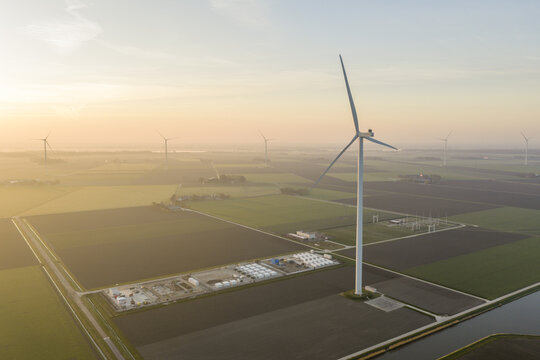 Aerial view of wind turbines generate clean renewable energy, with battery storage units in a rural landscape at sunset, emphasizing sustainable power
