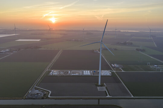 Aerial view of wind turbines generating clean energy at sunrise, connected to large battery storage units in the dutch agricultural landscape