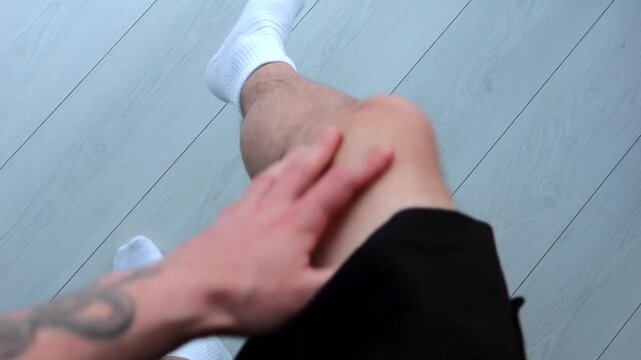 An itchy leg on a man in white socks.
A man stands on a white wooden floor and scratches his legs.