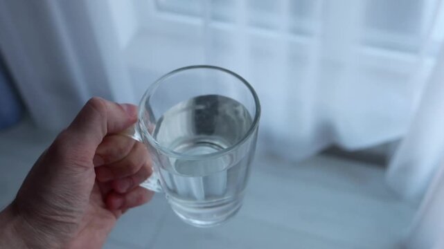 A man walks around the room in white socks with a cup of drinking water