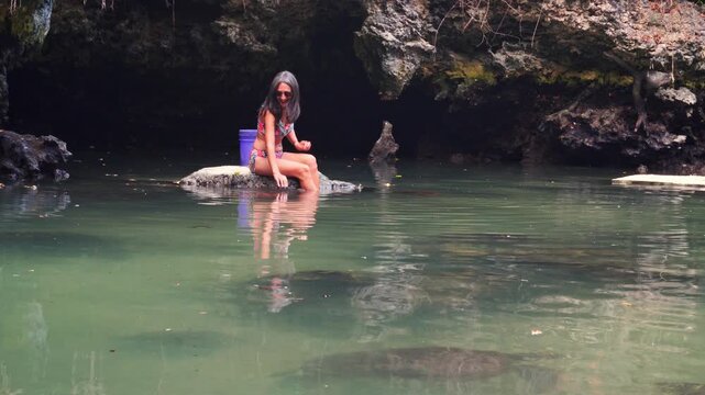 Woman swimming alongside rescued green sea turtles in the natural tidal pool of Baraka Natural Aquarium. High-angle view showcasing gentle marine life interaction in Zanzibar