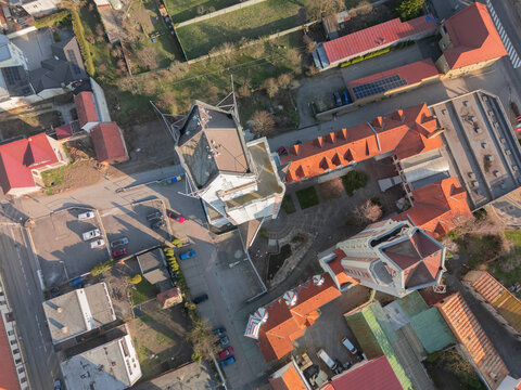 Aerial view of architectural contrasts where modern angles meet the historical curves of the church beneath a golden light, Lucenec, Banska Bystrica Region, Slovakia.