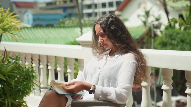 Woman writes peacefully. Focused female author works amidst lush foliage and gentle light. Calm woman carefully revises her manuscript surrounded by tropical palm leaves and soft sunlight