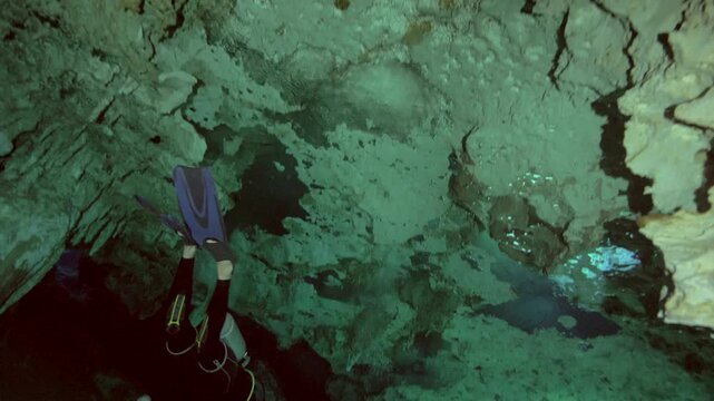 A diver is seen below a textured cave ceiling as the camera tilts downward in a submerged cavern in Cenote Dos Ojos, Quintana Roo