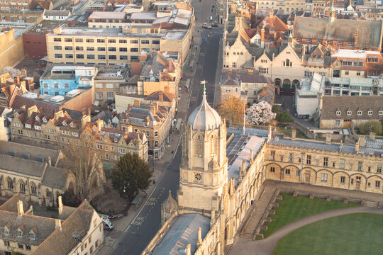 Aerial view of golden sunlight bathing the historic Christ Church College tower and cobbled streets in Oxford, England, casting long shadows across manicured lawns, Oxford, England, United Kingdom.