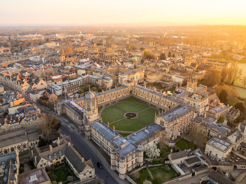 Aerial view of golden light bathes the ancient stone buildings of Oxford University, casting long shadows across the manicured lawns, Oxford, England, United Kingdom.