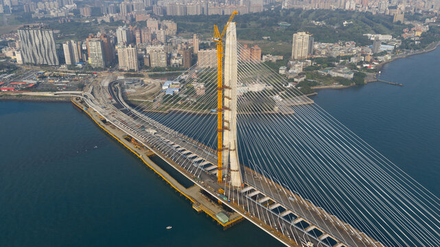 Aerial view of the Tamsui-Tamsui Bridge cable-stayed bridge under construction, its soaring yellow support contrasting with the blue waters, New Taipei City, Taiwan.