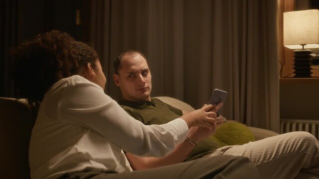 Medium shot of happy young woman chatting with her husband while they fooling around on sofa in living room