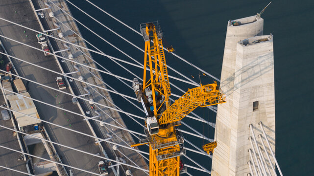 Aerial view of a vibrant yellow crane poised against the stark concrete of the Tamsui-Tamsui Bridge under construction, Shalun Road, New Taipei City, Taiwan.