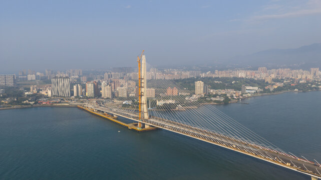 Aerial view of the Tamsui-Tamsui Bridge, a cable-stayed marvel under construction, stretches across the tranquil waters, contrasting with the urban skyline, Tamsui, New Taipei City, Taiwan.