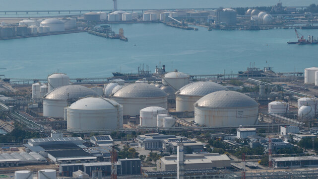 Aerial view of a vast industrial landscape with white storage tanks contrasting against the blue sea and sky, Tambon Map Ta Phut, Chang Wat Rayong, Thailand.