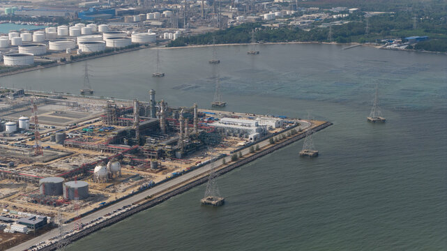 Aerial view of industrial structures meet the sea, a stark contrast of human engineering against nature's vastness, Tambon Map Ta Phut, Chang Wat Rayong, Thailand.
