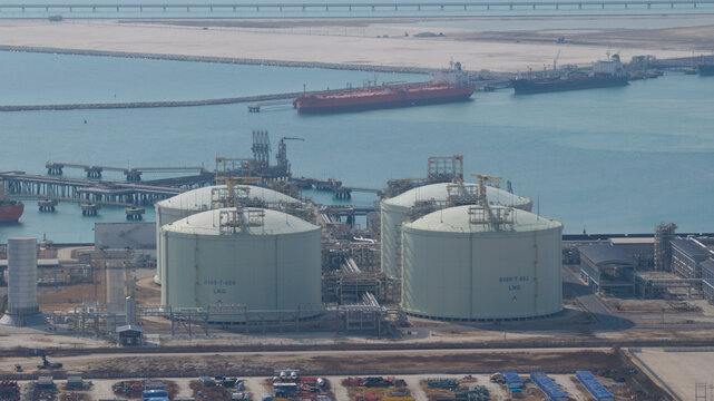 Aerial view of massive storage tanks gleaming under the sun near a bustling port with ships, a scene of industrial might, Tambon Map Ta Phut, Chang Wat Rayong, Thailand.