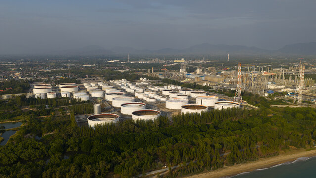 Aerial view of industrial tanks gleam white against the lush green coastline, where land meets sea in a symphony of industry and nature, Tambon Map Ta Phut, Thailand.