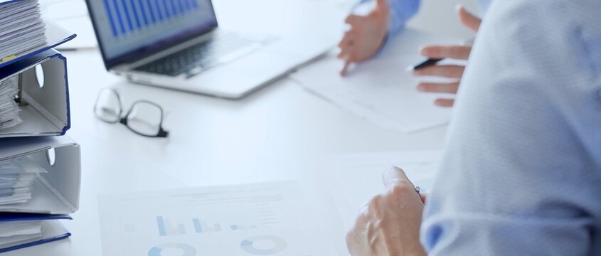 Group of accountants are analyzing financial reports and making notes while sitting at a white table, close up of a stack of blue folders full of paperwork. Audit and taxes in business