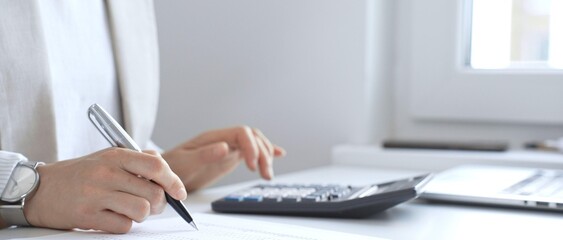 Fototapeta premium Businesswoman is calculating annual tax using calculator and taking notes in the office, managing domestic budget and checking financial documents. Audit and taxes in business