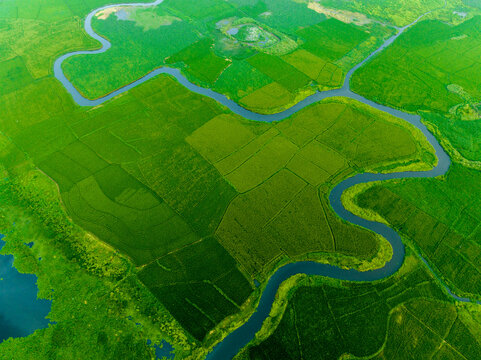 Aerial view of a winding river snaking through a vibrant landscape of lush green fields, creating a stunning natural contrast, Dhaka, Dhaka Division, Bangladesh.